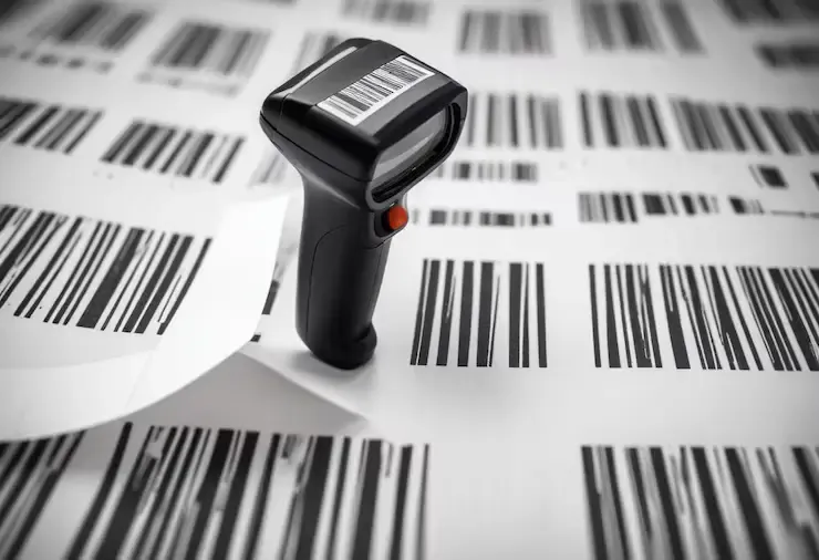 A handheld barcode scanner standing on sheets of printed barcodes